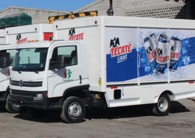Several parked small delivery trucks lined up displaying their Tecate Light Vehicle Wraps.